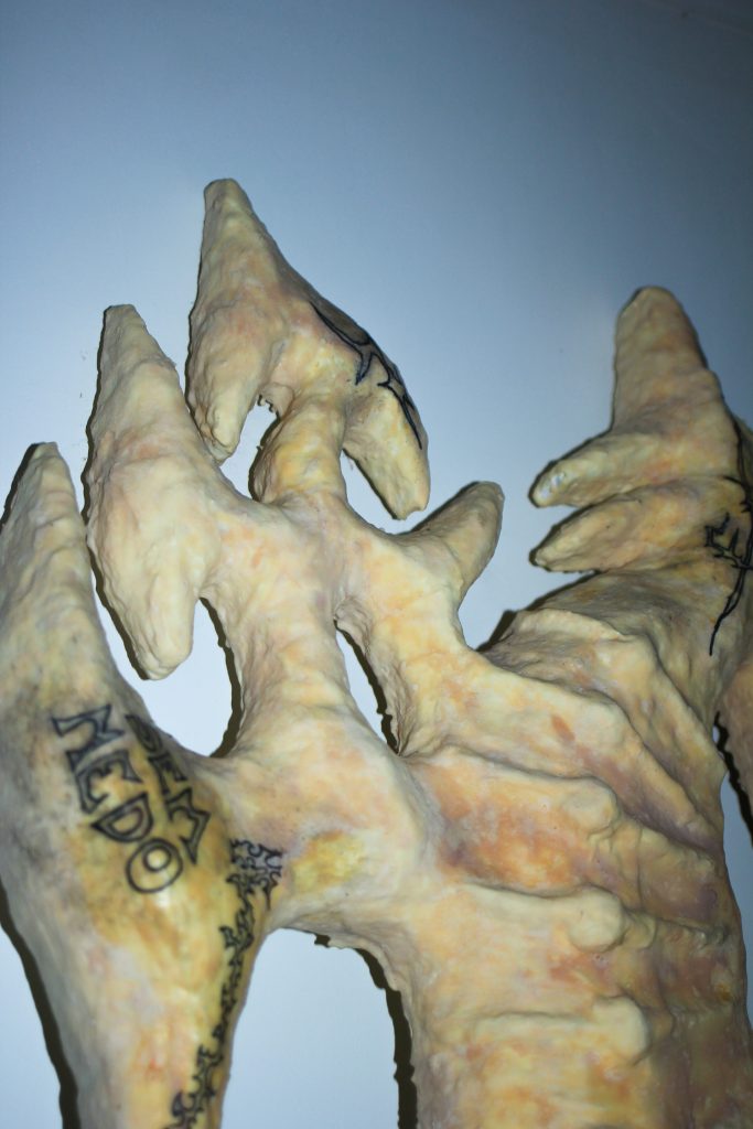 Detalhe de escultura com relevos texturizados e padrões orgânicos tatuados em tinta, evocando a estética do erro.