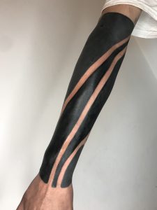 Braço tatuado em estilo Blackout com padrões vazados.