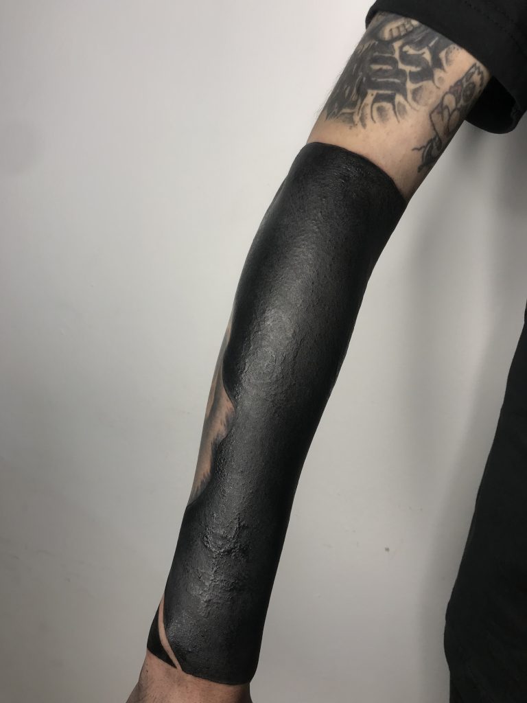 Tatuagem blackout cobrindo antebraço da artista Cahschu